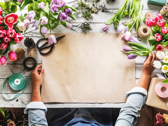 Papier wird zwischen Blumen auf einen Tisch gelegt.